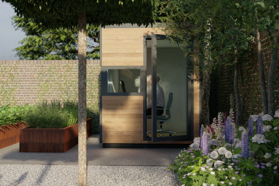 A person sits in a small, modern wooden eDEN Hub with large windows, situated in a garden with flowers, shrubs, and a brick wall, enjoying the perfect home office for working-from-home.